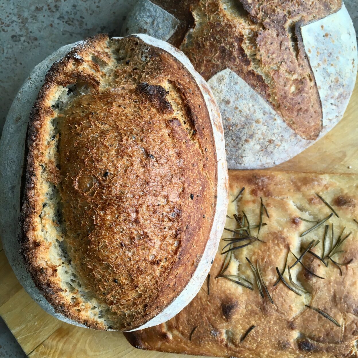 Loaves of crusty sourdough bread with herby focaccia on a brown board - create your own at my sourdough classes in Surrey, including sourdough demos
